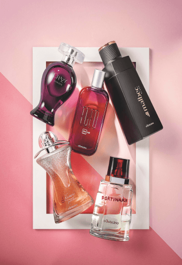 São 5 perfumes O Boticário sobre uma moldura branca e fundo rosa, como se fosse um quadro. Os perfumes são Crazy, Malbec, Portinari, Egeo e Glamour Just Shine