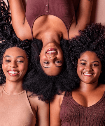 3 mulheres negras maquiadas deitadas no chão utilizando batons em tons de vermelho